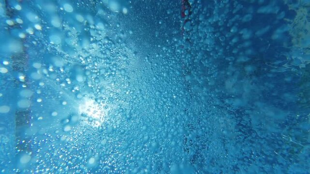 Underwater view of air bubbles and sunlight on swimming pool surface