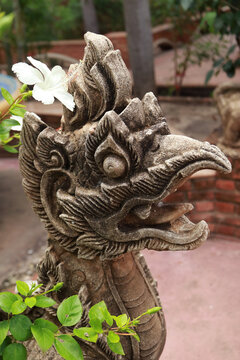 Close-up of ancient Chinese mythical creature stone sculpture adorned with a white flower in a garden of Wat Na Phra Meru temple, Ayutthaya