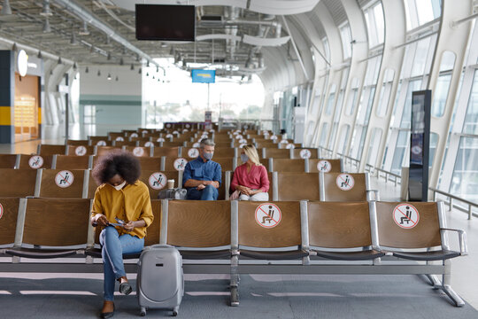 Passengers maintain physical distance while waiting for their flights, with social distancing markers visible on the seats