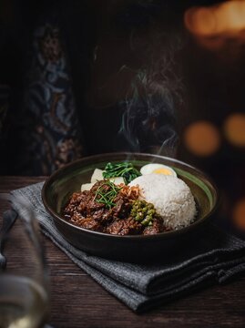 Nasi Rendang. Nasi Rendang daging sapi. Indonesian Beef Rendang with Rice. Nasi Rendang Dark Moody Smoke. Delicious Indonesian Beef Rendang with Rice Served in Ceramic Bowl on Dark Wooden Table