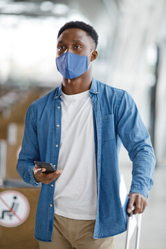 A man wearing a protective face covering walks through an airport terminal with his phone and travel documents