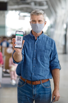 A middle-aged man with graying hair holds up his mobile phone displaying a digital health pass for travel or entry