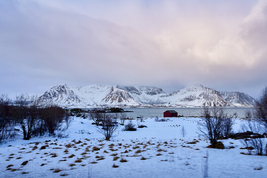 Beautiful scenic viewpoint of an iconic concrete bridge crossing the blue sea fjord in Lofoten, Norway. Majestic winter landscape with grand snow-covered mountains under a dramatic sky in Arctic Scand