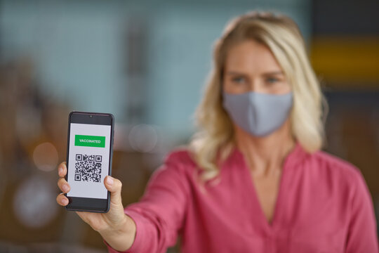 A woman wearing a protective face mask displays a digital vaccination certificate on her smartphone screen