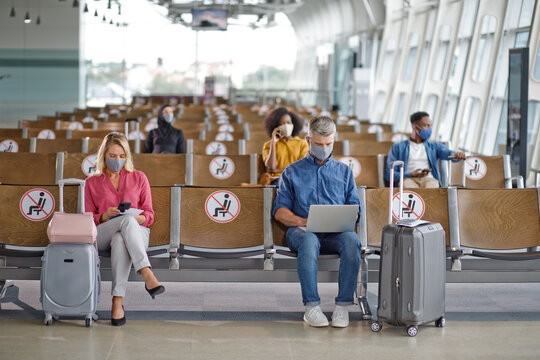 Travelers maintain distance in airport seating area, adhering to safety protocols during a pandemic with masks on