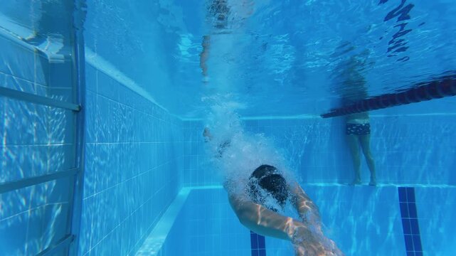 Slow motion underwater view of teenager diving headfirst into swimming pool