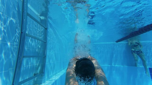 Slow motion underwater view of teenager diving headfirst into swimming pool
