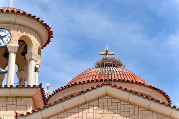 Large stork nest built on the red tiled dome around a golden cross of an Orthodox church in Greece © RayBreen