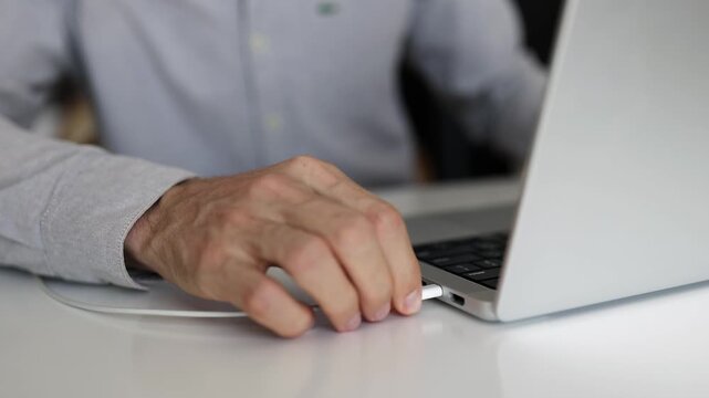 Man connecting usb-c cable to laptop at home office.