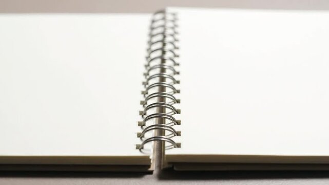 Close-up view of a blank notebook opened with white pages and spiral binding on a neutral surface