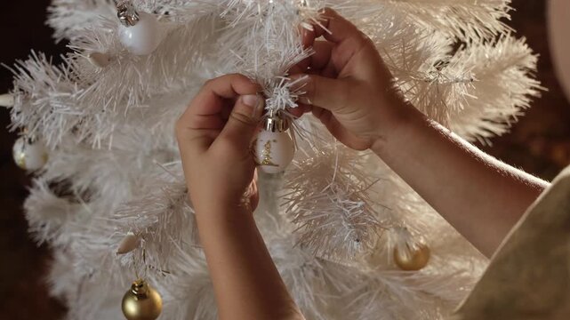 Child decorating white Christmas tree with Christmas ornaments