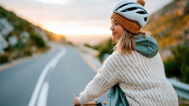 The captivating image portrays a woman cycling down a scenic road, embracing the freedom and serenity of the sunset, establishing a connection with nature and outdoor adventure.