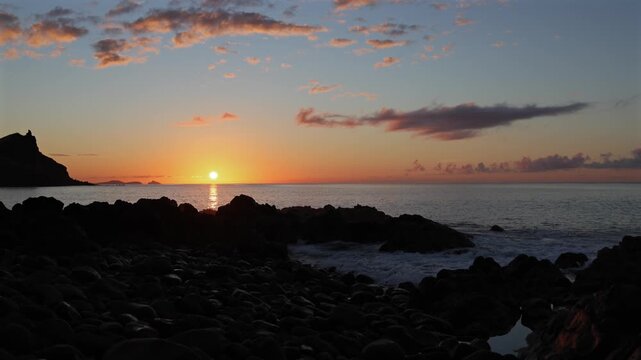 Scenic golden sunset over the rugged volcanic coastline and Atlantic Ocean in Madeira, capturing tranquil waves and dramatic evening clouds in cinematic motion. 4K video.