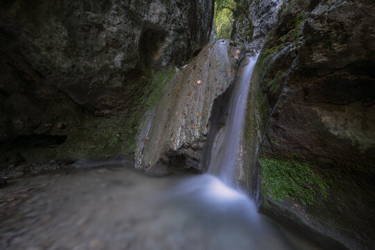 A serene long exposure shot of a waterfall tucked inside a shaded, mossy canyon, perfect for wellness and nature backgrounds.