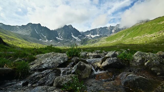 Rocky stream flowing through green alpine valley with mountains