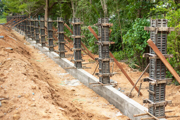 Naklejka premium Fresh foundation work lines earthy slope with concrete footing, stacked form columns, and timber bracing. Forms stand in sequence beside trench, creating orderly structural support along site edge.