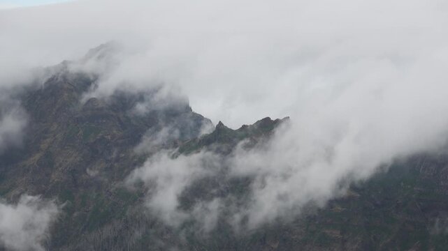 Dramatic mist and low clouds moving over rugged volcanic mountain peaks in Madeira, creating an ethereal atmospheric alpine landscape with moody light. 4K video.