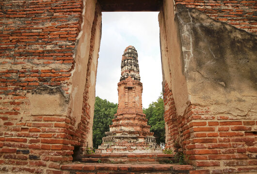 Creative framing shot of ancient Prang chedi viewed through the brick doorway of ruined ordination hall at Wat Borom Phuttharam, Ayutthaya, Thailand