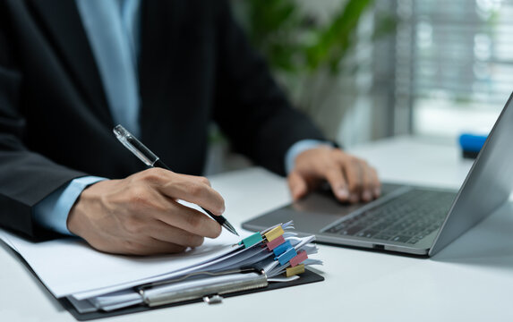 Businessman reviewing organized documents with colored tabs beside a laptop, representing office administration, paperwork, reporting, documentation and corporate workflow.