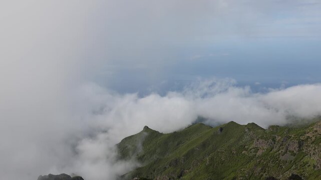 Scenic aerial view of green mountain ridges surrounded by thick white clouds in Madeira, capturing a peaceful, dramatic wilderness landscape under soft light. 4K video.