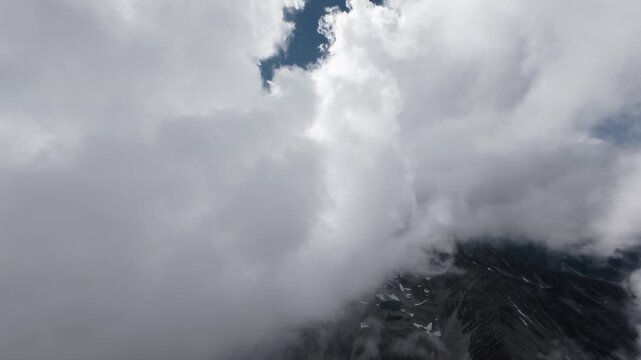 Aerial camera moving through thick clouds above mountains