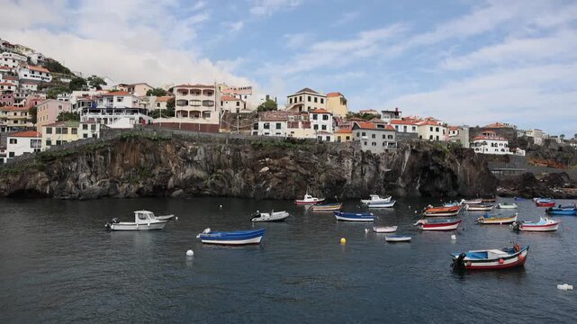 Scenic view of colorful traditional fishing boats moored in the harbor bay against volcanic cliffs and coastal village in Camara de Lobos, Madeira island. 4K video.
