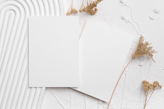 Blank white stationery cards positioned on textured background with dried flowers and abstract shapes, ideal for mockup designs and creative presentations