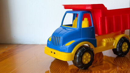 A plastic toy dump truck with red and yellow cargo bed standing on a wooden surface, children playroom toy. © Анна Трегубова