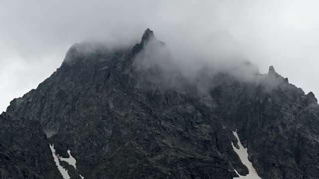 Clouds drifting across rocky alpine mountain peak
