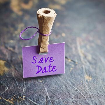 Purple paper note with save date text held by a wooden clothespin announcement reminder stationery textured selective handwritten