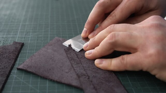 Close-up of a craftsman's hands carefully thinning the edge of a piece of genuine leather with a special knife on a cutting mat