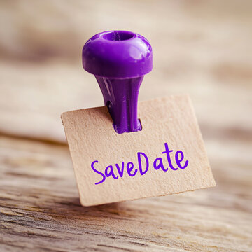 Kraft paper tag with save date text held by a purple plastic announcement reminder stationery selective handwritten celebration romantic