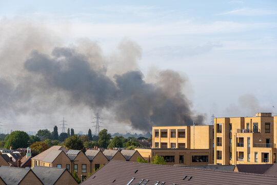Thick Black Smoke Rising Over Residential Area on Clear Day with Modern Buildings