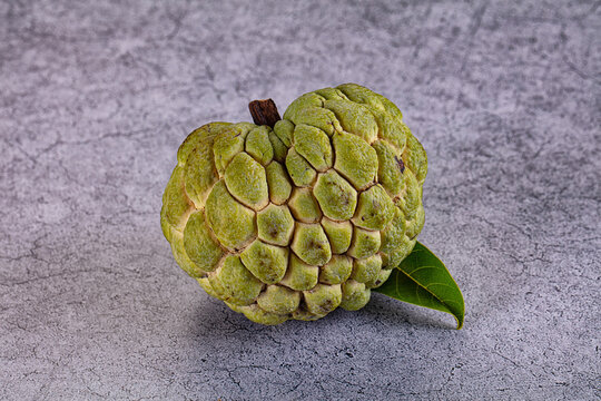 Green custard apple with leaf on textured gray surface