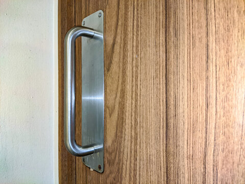 Metal door handle mounted on a wood-pattern HPL door, combining durability and modern design, highlighting clean lines and functional detail in a contemporary interior setting.