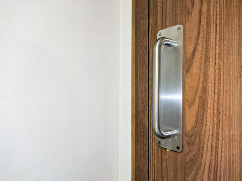 Metal door handle mounted on a wood-pattern HPL door, combining durability and modern design, highlighting clean lines and functional detail in a contemporary interior setting.