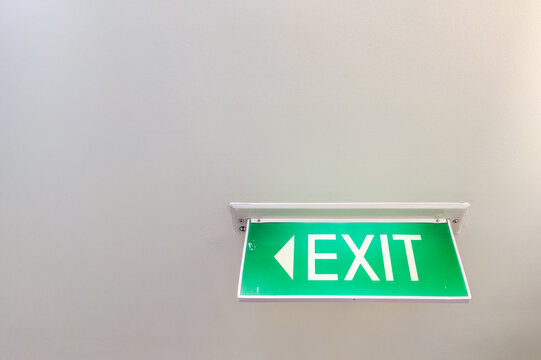 Green illuminated EXIT sign mounted on a corridor ceiling, providing clear emergency wayfinding and directional guidance for people inside a modern building.