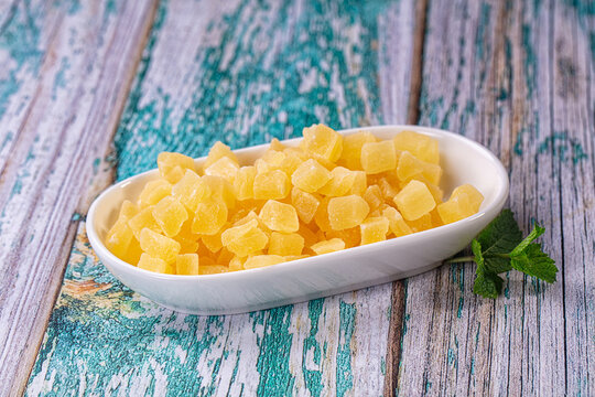 Dried pineapple chunks in white bowl on rustic wooden surface with mint sprig