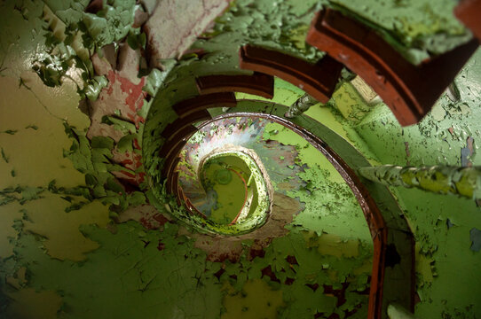 Abandoned overgrown mansion with spiral staircase, old car and ruined interior