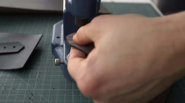 Craftsman installing a metal rivet on genuine leather using a hand press machine in a workshop