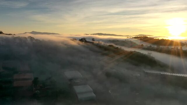 Aerial sunrise over Trai Mat, Xuan Truong Ward, Da Lat, Lam Dong, Vietnam, with drifting mist, clouds and golden sunlight illuminating the peaceful highland landscape.