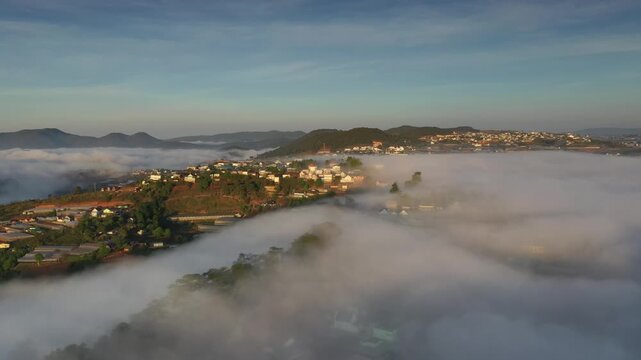 Aerial sunrise over Trai Mat, Xuan Truong Ward, Da Lat, Lam Dong, Vietnam, with drifting mist, clouds and golden sunlight illuminating the peaceful highland landscape.
