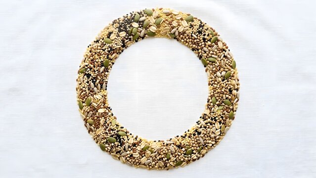 Overhead view of a circular arrangement of mixed seeds and grains on a white textured background