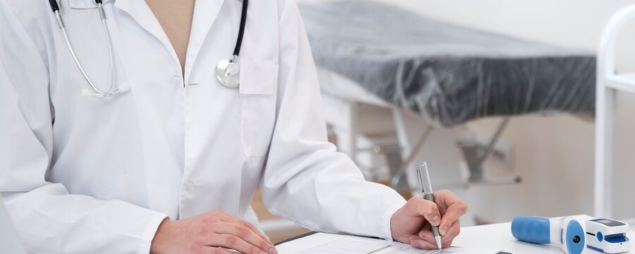 Doctor in white coat writing notes with examination table and test tubes in background