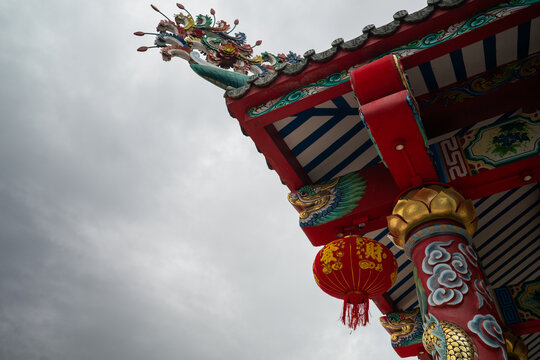 Traditional Chinese temple roof architecture with colorful dragon carvings and hanging red lantern under cloudy sky.