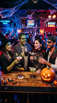 Friends in costumes celebrate Halloween at a bar with spooky drinks, a carved pumpkin, and cobwebs, representing a festive celebration.