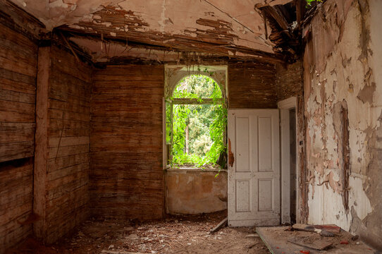 Abandoned overgrown mansion with spiral staircase, old car and ruined interior