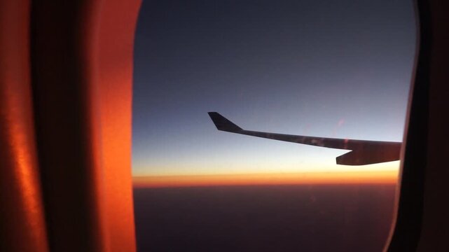 Stunning horizontal view from airplane window featuring jet wing flying above golden orange clouds during serene evening sunset flight concept for commercial travel advertisement and background
