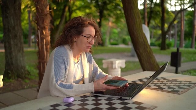 Woman working on laptop while sitting at a table in a park during sunset
