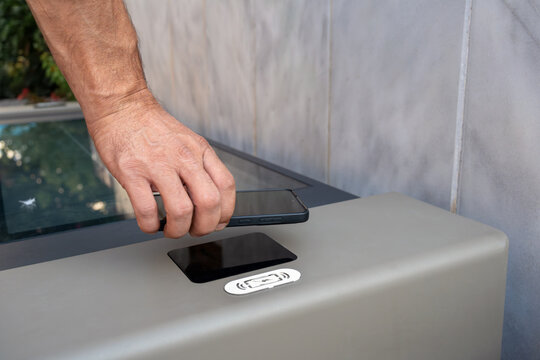 Man places smartphone on wireless charging pad built into solar-powered public smart bench, illustrating convenient mobile technology, renewable energy and innovative urban infrastructure